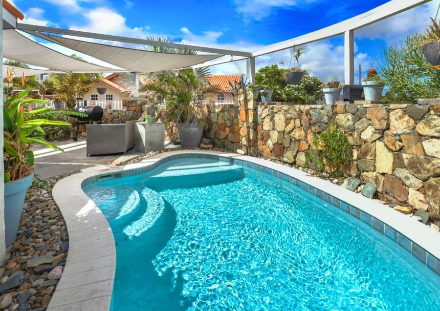 The private pool beside a stone garden wall under white shade sails